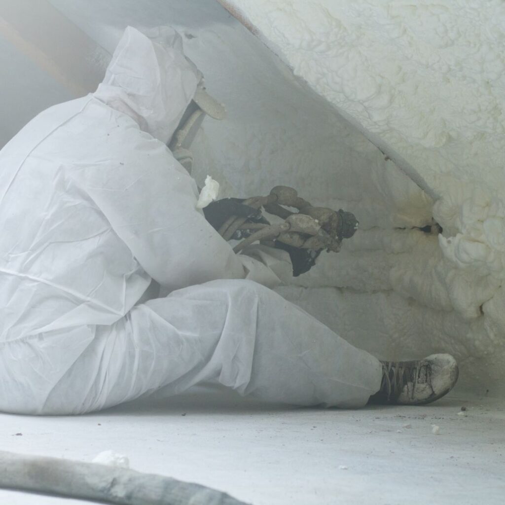 a worker spraying foam insulation in a crawlspace
