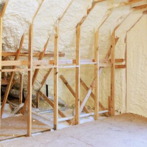 An unfinished attic wall with exposed wood framing completely filled with thick, off-white spray foam insulation.