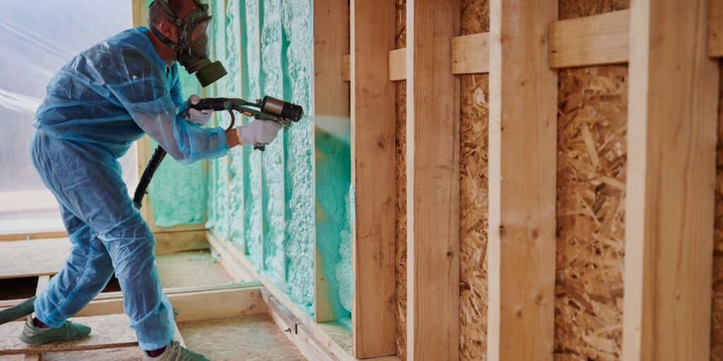 A Pro-Seal Spray Foam professional in full protective gear applies high-performance spray foam insulation to a wall cavity.