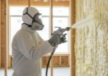 A Pro-Seal technician in a full protective suit and respirator applies spray foam insulation to a wall in a new construction home.