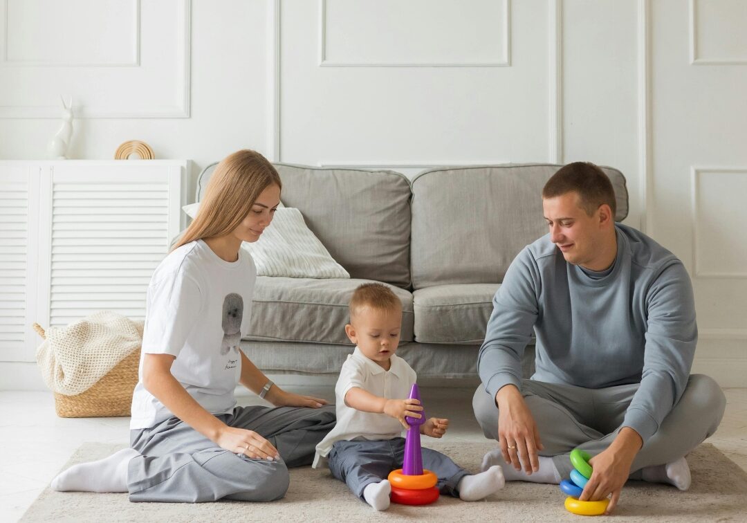 A happy young family with a toddler plays comfortably on the floor of their well-insulated living room.
